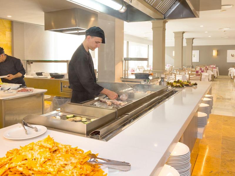 Hotelkeuken met een kok die werkt bij een groot fornuis in een modern ontbijtgedeelte.