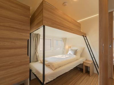 Modernes Hotelzimmer mit einem Hochbett aus Holz und Metall, darunter ein gemütliches Einzelbett.