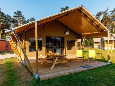 Modernes, gelbes Zelt mit Terrasse und Picknicktisch in waldreicher Umgebung.