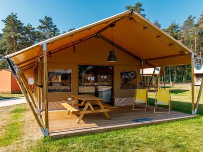 Ein modernes Holz- und Zelt-Hotelgebäude mit Terrasse und Picknicktisch auf Rasen vor Wald.