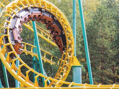 Gelbe Achterbahn mit Looping in einem von Bäumen umgebenen Freizeitpark.
