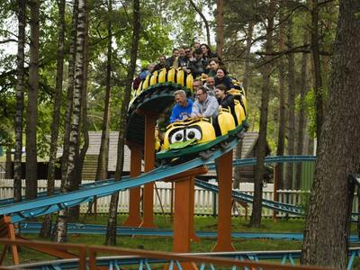 Achterbahn mit fröhlichen Fahrgästen, die durch einen Wald fahren.