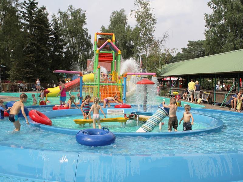 Kinder spielen in einem großen, blauen Wasserpool mit bunten Rutschen und Wasserspielen im Freien.