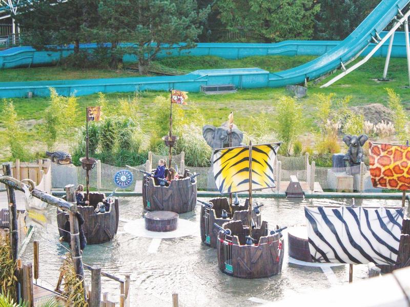 Kinderbootfahrt mit Safari-Themen in einem Wasserpark mit Rutschen im Hintergrund.