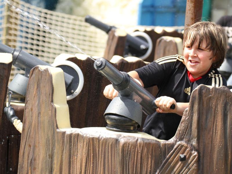 Kind spielt mit Kanonenattrappe auf einem Holzspielplatz bei einer Urlaubsaktivität.