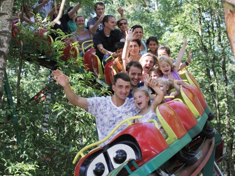 Menschen fahren auf einer bunten Achterbahn durch einen bewaldeten Park.