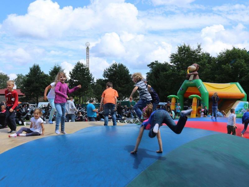 Kinder spielen auf einem großen, bunten Hüpfkissen im Freien an einem sonnigen Tag.