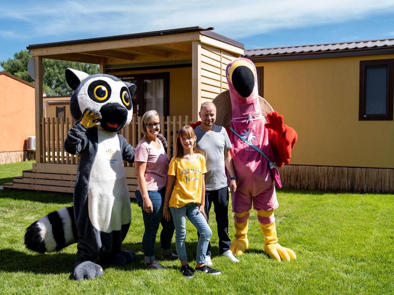 Familie posiert mit zwei Personen in Tiermaskottchen-Kostümen vor einem Mobilheim.