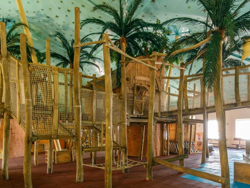 Innenbereich mit Baumhaus und Palmen im tropischen Hotelspielbereich.