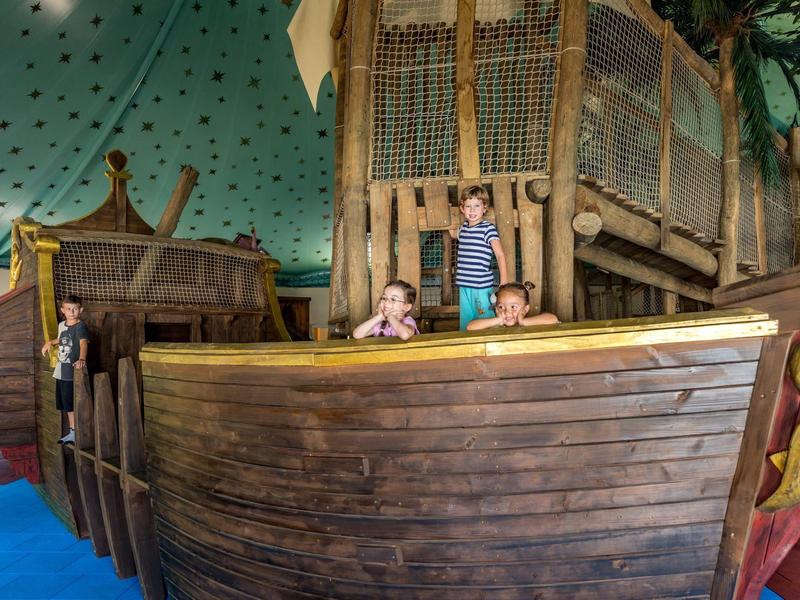 Kinder spielen auf einem großen hölzernen Piratenschiff im Innenbereich.