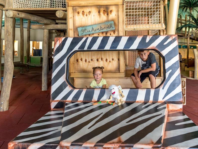 Kinder spielen in einem großen, gepolsterten Klettergerüst mit gestreiften Mustern im Innenbereich.