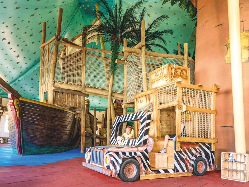 Innenbereich mit künstlichem Wasser, Holzboot und Safari-Buggy, tropisch dekoriert.