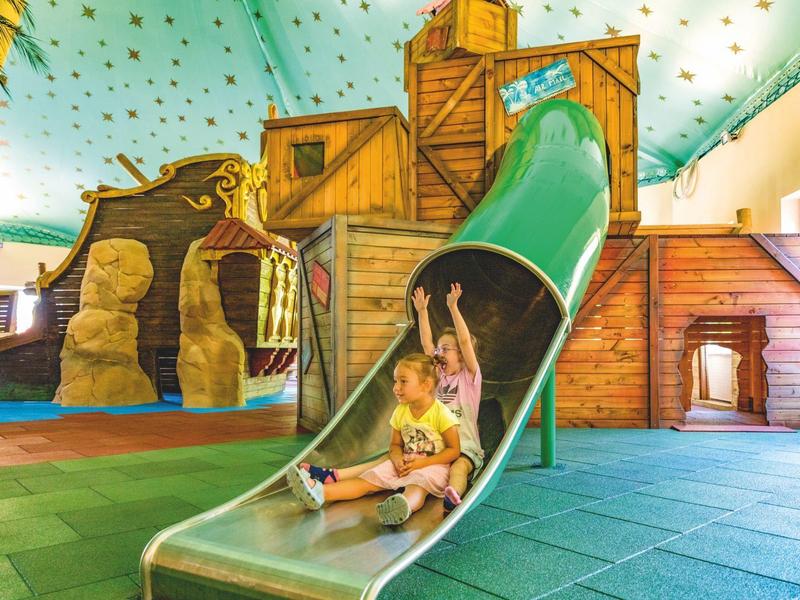 Kinder rutschen auf einer Rutsche in einem bunten Indoor-Spielplatz im Hotel.