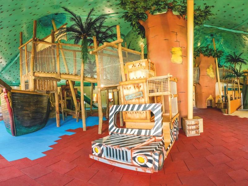 Innenraum eines tropischen Hotel-Lobbies mit luftiger Holzdeko und buntem Bodenbelag.