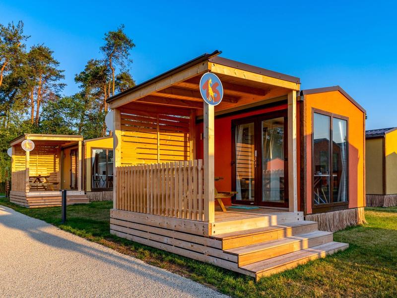 Moderne Holzhäuser mit Veranden unter klarem blauem Himmel in einer Urlaubssiedlung.