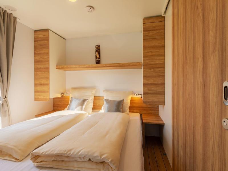 Helles Hotelzimmer mit Doppelbett, Holzmöbeln und Fenster mit Vorhängen.