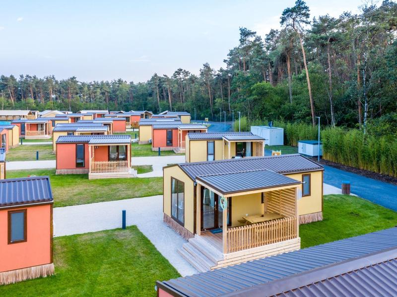Feriendorf mit modernen, bunten Holzhäusern in waldreicher Umgebung unter blauem Himmel.