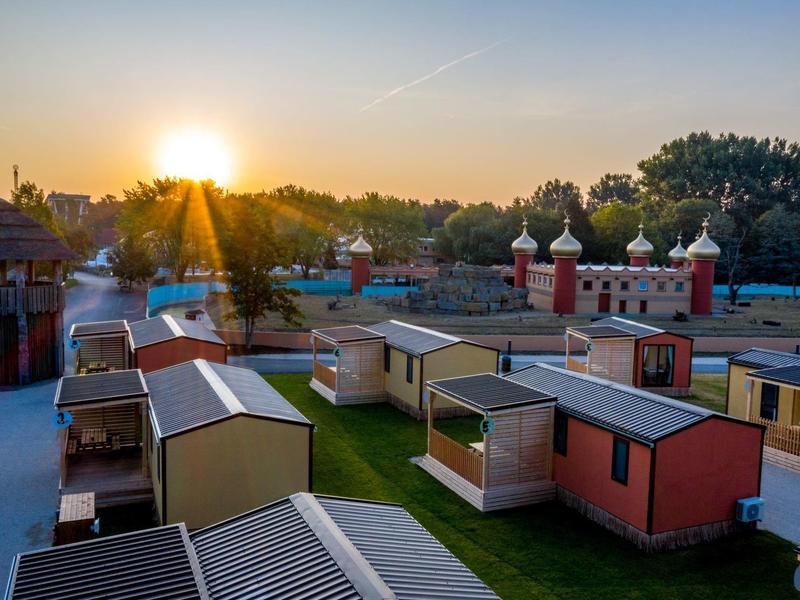 Sonnenuntergang über bunten Ferienhäusern in einer Parkanlage mit grünen Rasenflächen.