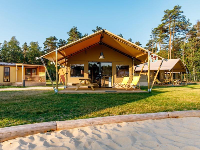 Zelte mit Terrasse auf grünem Rasen neben einem Sandbereich und Bäumen im Hintergrund.