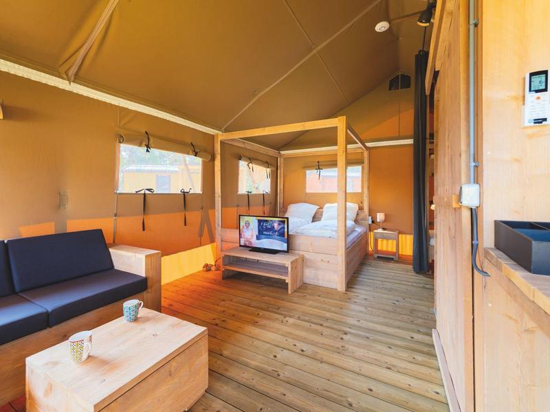 Geräumige Zeltlodge mit Holzinterieur, einem Bett, Sofa und gemütlicher Atmosphäre.