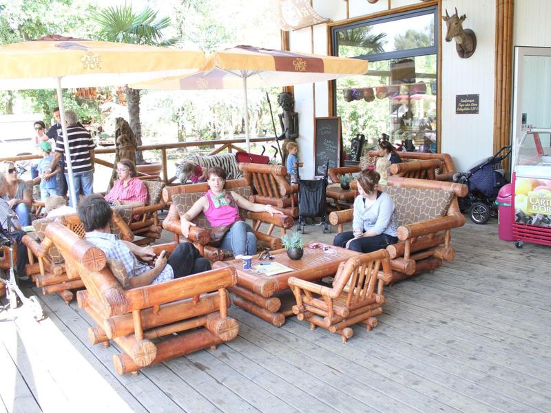 Mehrere Personen sitzen auf hölzernen Gartenmöbeln unter Sonnenschirmen auf einer Terrasse.