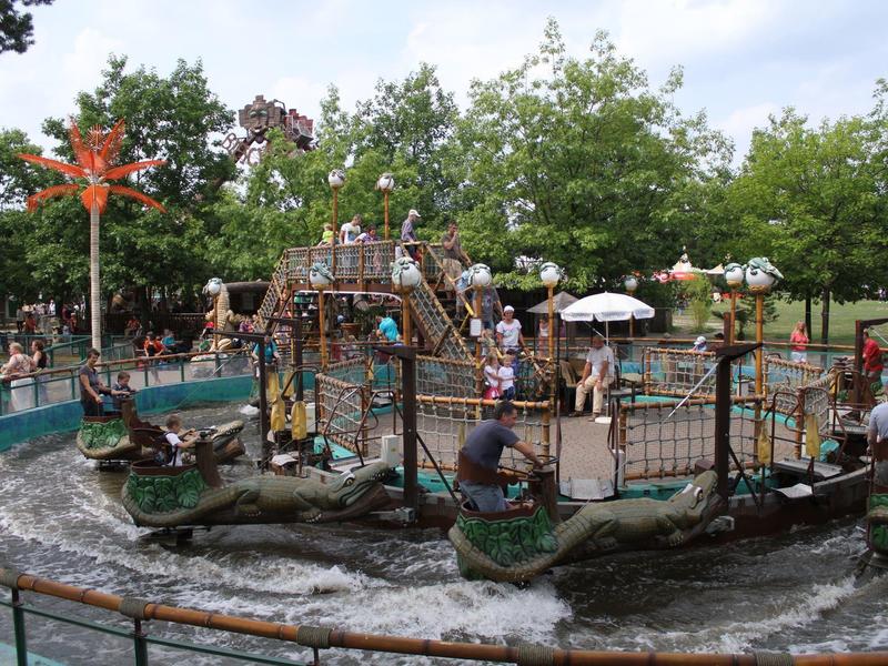 Wasserspielplatz mit Booten und Rutschen in einem grünen Park bei sonnigem Wetter.