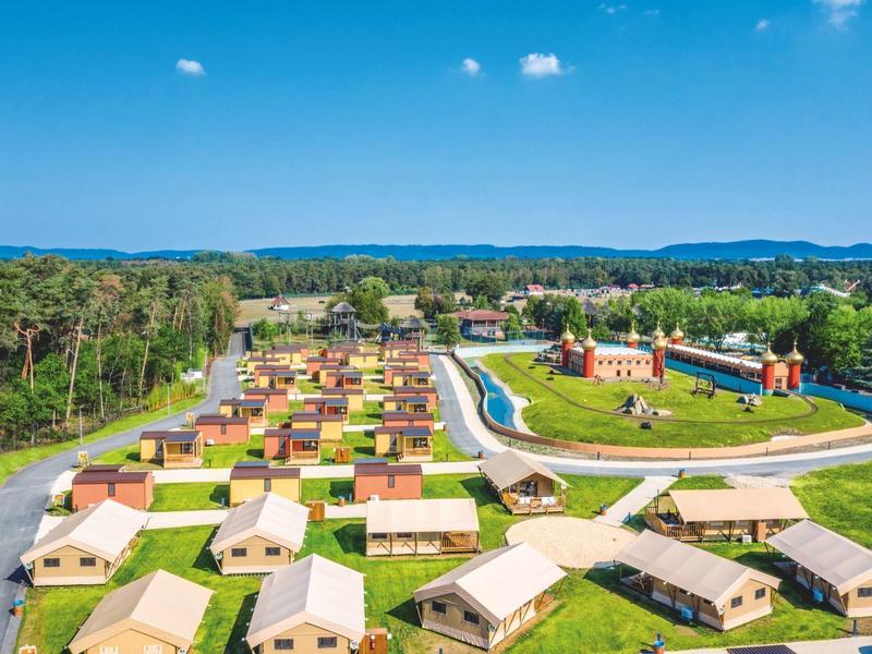 Luftaufnahme eines Campingplatzes mit vielen kleinen Hütten, Pool und umliegender Natur.