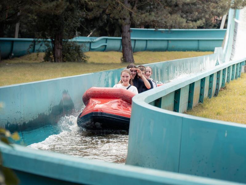 Zwei Personen fahren in einem roten Boot auf einer Wasserbahn im Freizeitpark.