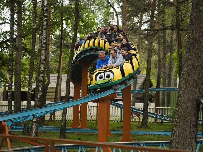 Achterbahn mit fröhlichen Fahrgästen, die durch einen Wald fahren.