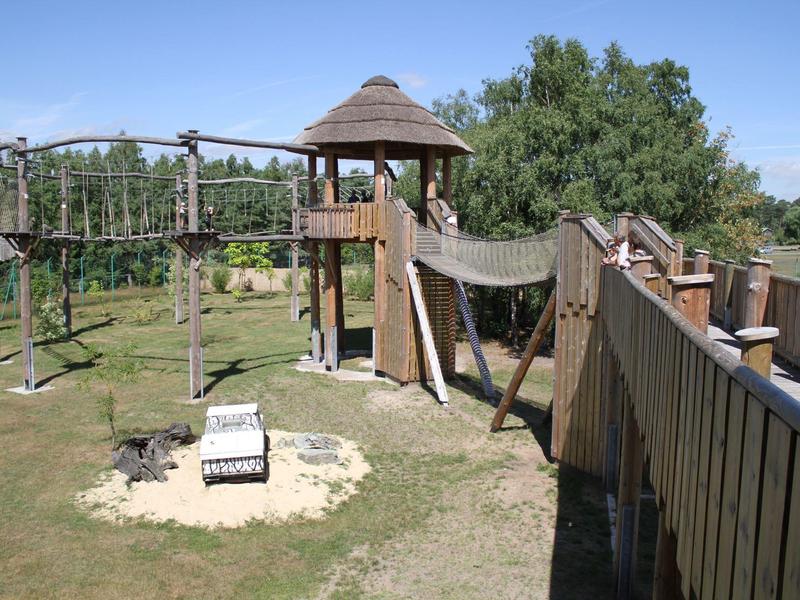 Abenteuer-Spielplatz mit Holzstruktur, Rutsche und Sandkasten in einer grünen Umgebung.