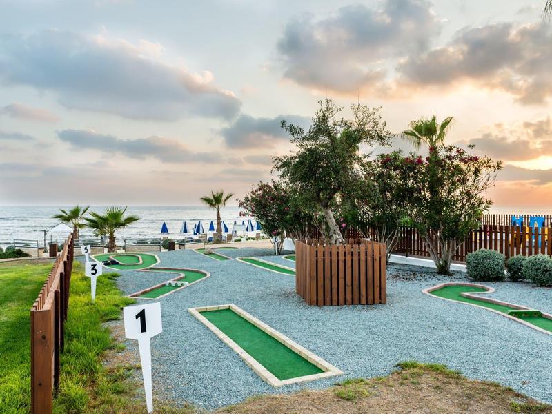 Minigolfanlage mit grünem Kunstrasen, weißen Zahlenmarkierungen und Palmen im Hintergrund am Abend.