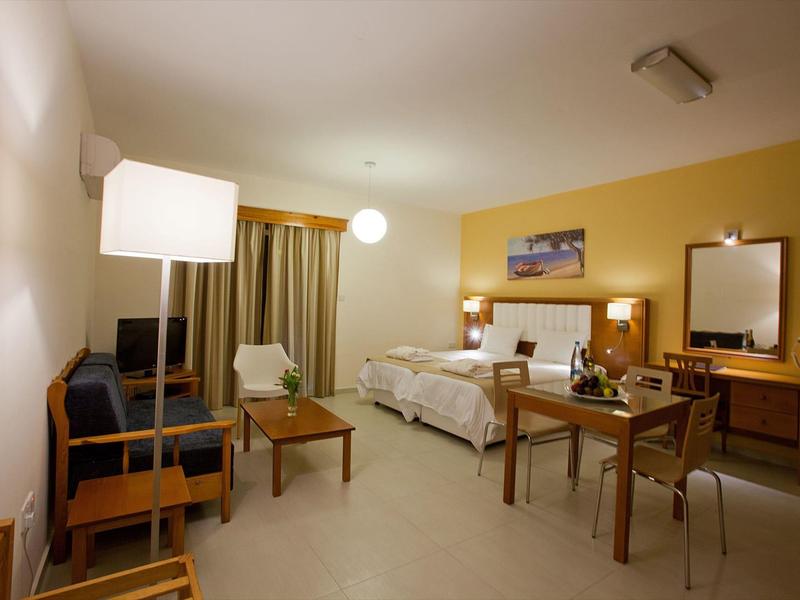 Hell eingerichtetes Hotelzimmer mit Doppelbett, Sitzgruppe, Schreibtisch und warmen gelben Wänden.