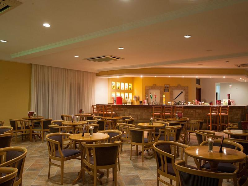 Leerer Gastronomiesaal mit rundem Tisch und Holzstühlen, beleuchtete Bar im Hintergrund.