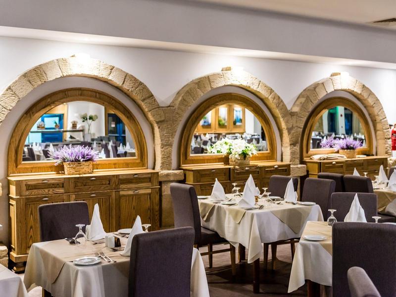 Elegantes Restaurant mit weißen Tischen, dunklen Stühlen und dekorativen Steinbögen an der Wand.