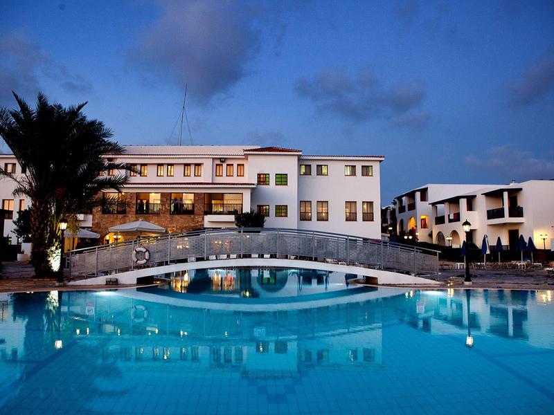 Großes Hotel mit weißer Fassade und beleuchtetem Pool bei Abenddämmerung.