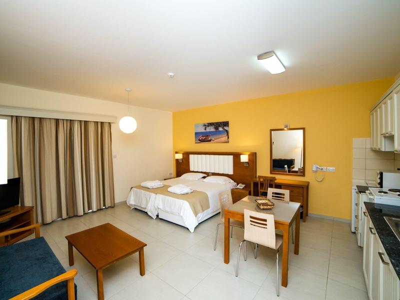 Helles Hotelzimmer mit gelber Wand, Doppelbett, Esstisch, Sofa und Küchenzeile.