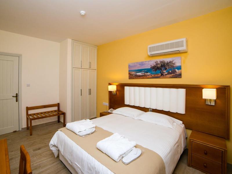 Schlafzimmer mit Doppelbett, gelber Wand, Luftklimaanlage, Nachttischen und einem gemalten Bild über dem Kopfteil.