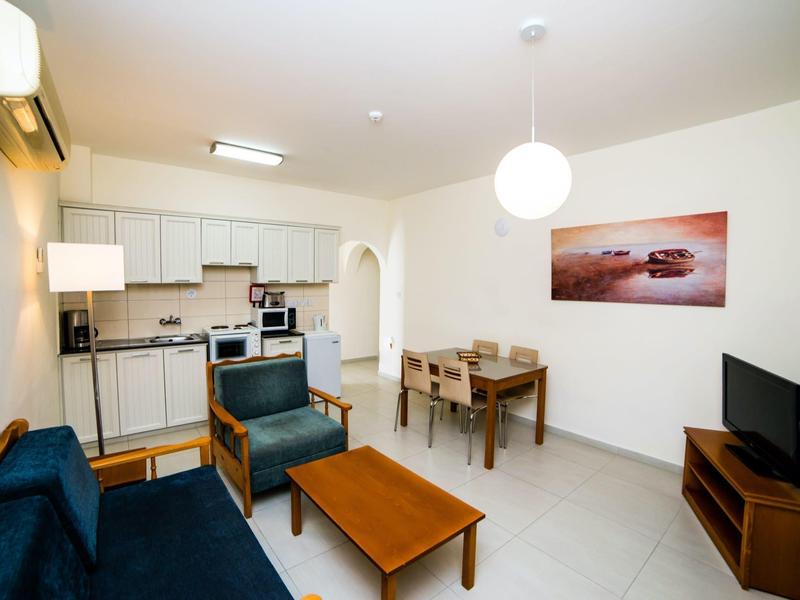 Helles Wohnzimmer mit blauem Sofa, Holzmöbeln, Esstisch und moderner Küchenecke.