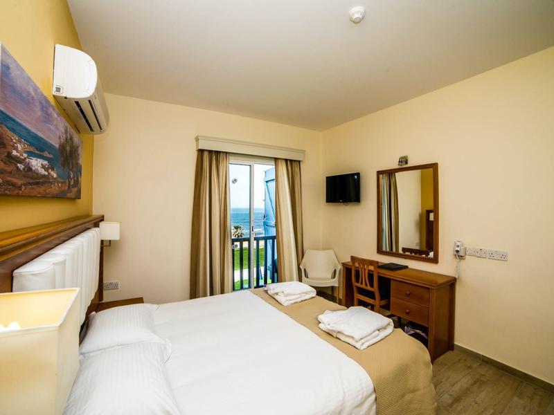 Helles Schlafzimmer mit Doppelbett, Wand-TV, Klimaanlage, Schreibtisch, kleinem Balkon und Vorhängen.