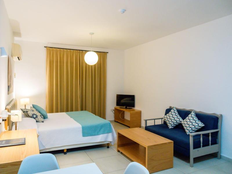 Hell eingerichtetes Schlafzimmer mit Doppelbett, blau-weißen Kissen und Holzmöbeln.