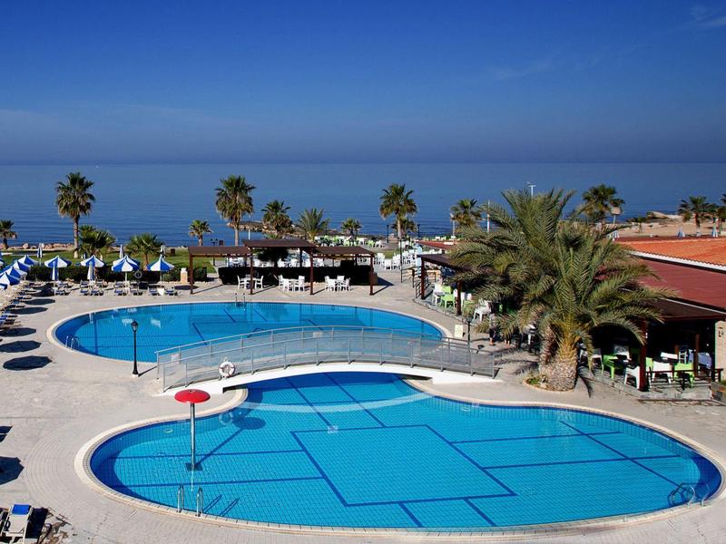 Zwei große Pools mit blauer Umrandung, Palmen und blauer Himmel am Meer im Hintergrund.