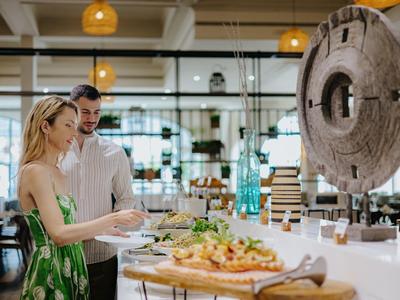 Ein Paar wählt Essen an einem Buffet in einem modernen, hellen Raum mit großen Fenstern.