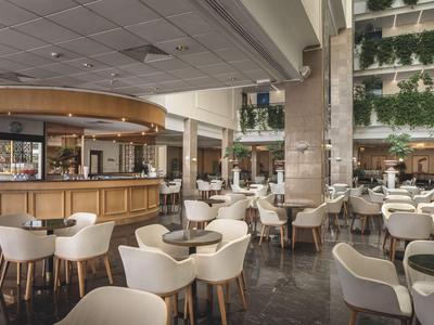Espace de restaurant d'hôtel moderne avec chaises blanches, tables en bois et décor végétal abondant.