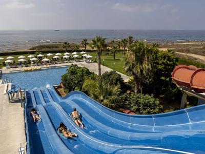 Glijbanen bij het hotelzwembad met uitzicht op zee en parasols op de achtergrond.