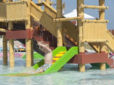 Kind glijdt van een groene glijbaan van een houten zwembadstructuur het water in.