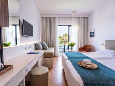Moderne hotelkamer met tweepersoonsbed, zithoek en balkon met uitzicht op groene omgeving.