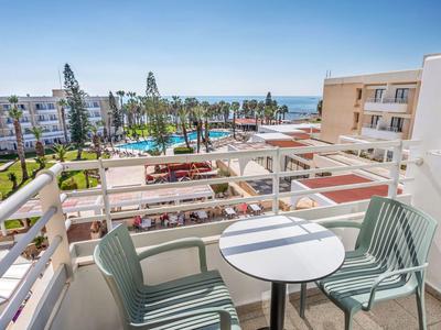 Balkon met twee stoelen en tafel met uitzicht op hotelzwembad, tuin en zee.
