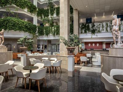Ruime hotel lobby met sculpturen, planten en moderne zitplaatsen in neutrale kleuren.