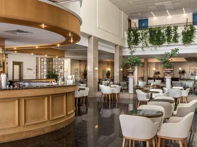 Licht hotelrestaurant met houten bar, witte stoelen en groene planten op het balkon.