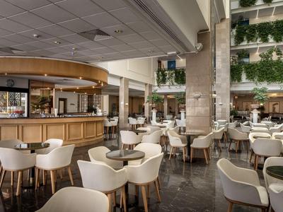 Elegantes Hotelcafé mit weißen Sesseln, Holztischen und grünen Pflanzen an den Wänden.
